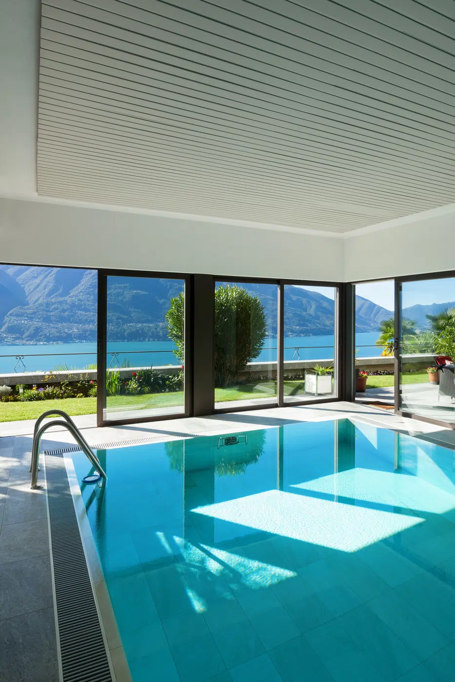 Modern glass-walled indoor pool pavilion overlooking lake and mountains