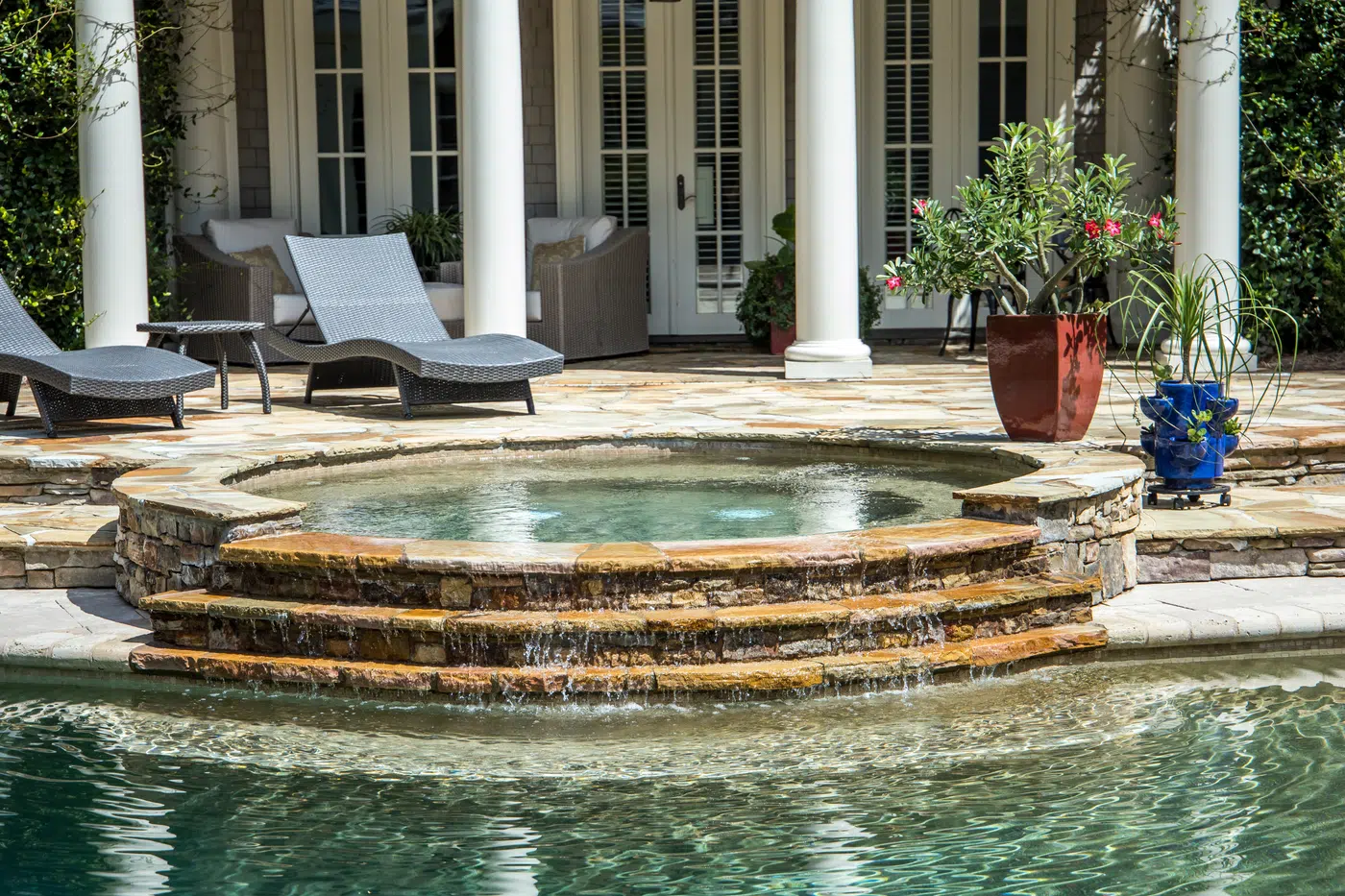 Classical estate terrace featuring a tiered stone spillover spa and pool